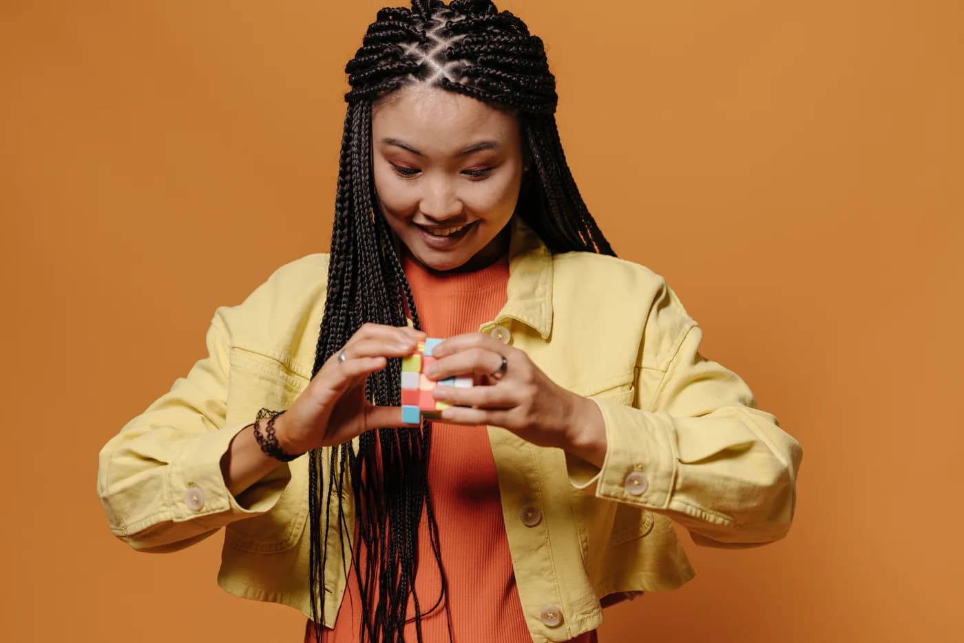 Someone in a yellow jacket smiling as they turn a colourful puzzle cube, against an orange background.
